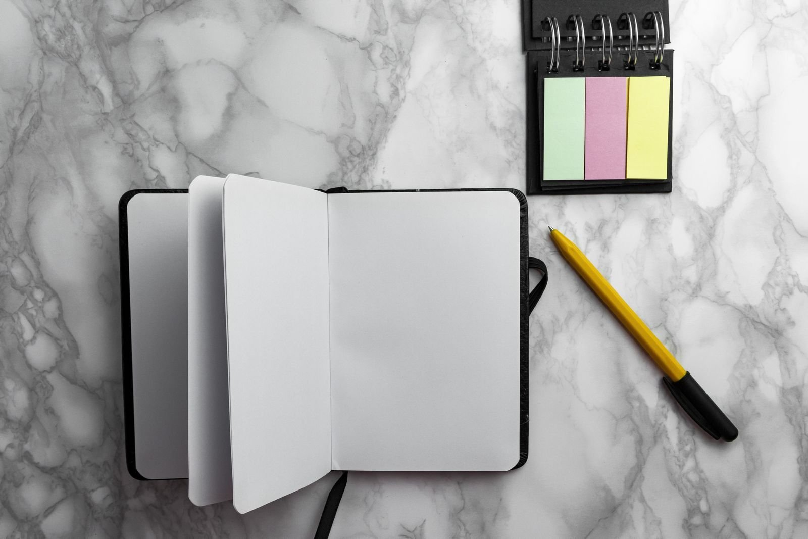 Fotografia de um caderno, caneta e blocos de notas adesivas sobre uma mesa.